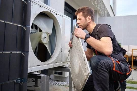 Technician inspecting the exposed fan of an outdoor heat pump